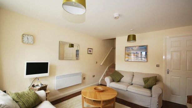 A living room with a sofa, a coffee table, a TV, a painting, a clock, and a staircase. - House Martins (Chathill)