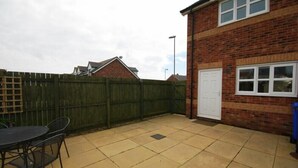 A patio with a table and chairs, a brick building with a garage, and a wooden fence. - House Martins (Chathill)