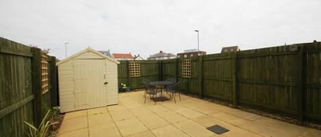A backyard with a patio, a shed, and a wooden fence.
