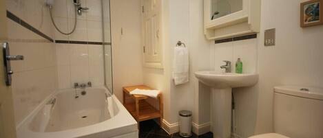 Et badeværelse med badekar, håndvask, toilet og en lille træskammel.
