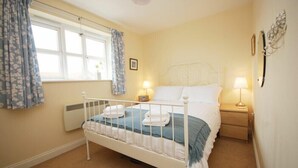 A bedroom with a single bed, bedside tables, a window with curtains, and wall-mounted decor. - House Martins (Chathill)