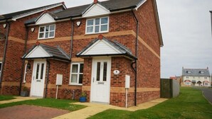 A two-story residential building with a brick facade, white-framed windows, and a small front garden. - House Martins (Chathill)