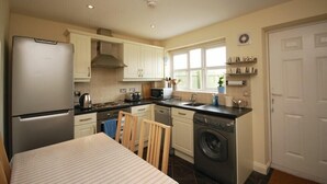 A compact kitchen with a refrigerator, stove, microwave, sink, and washing machine. - House Martins (Chathill)