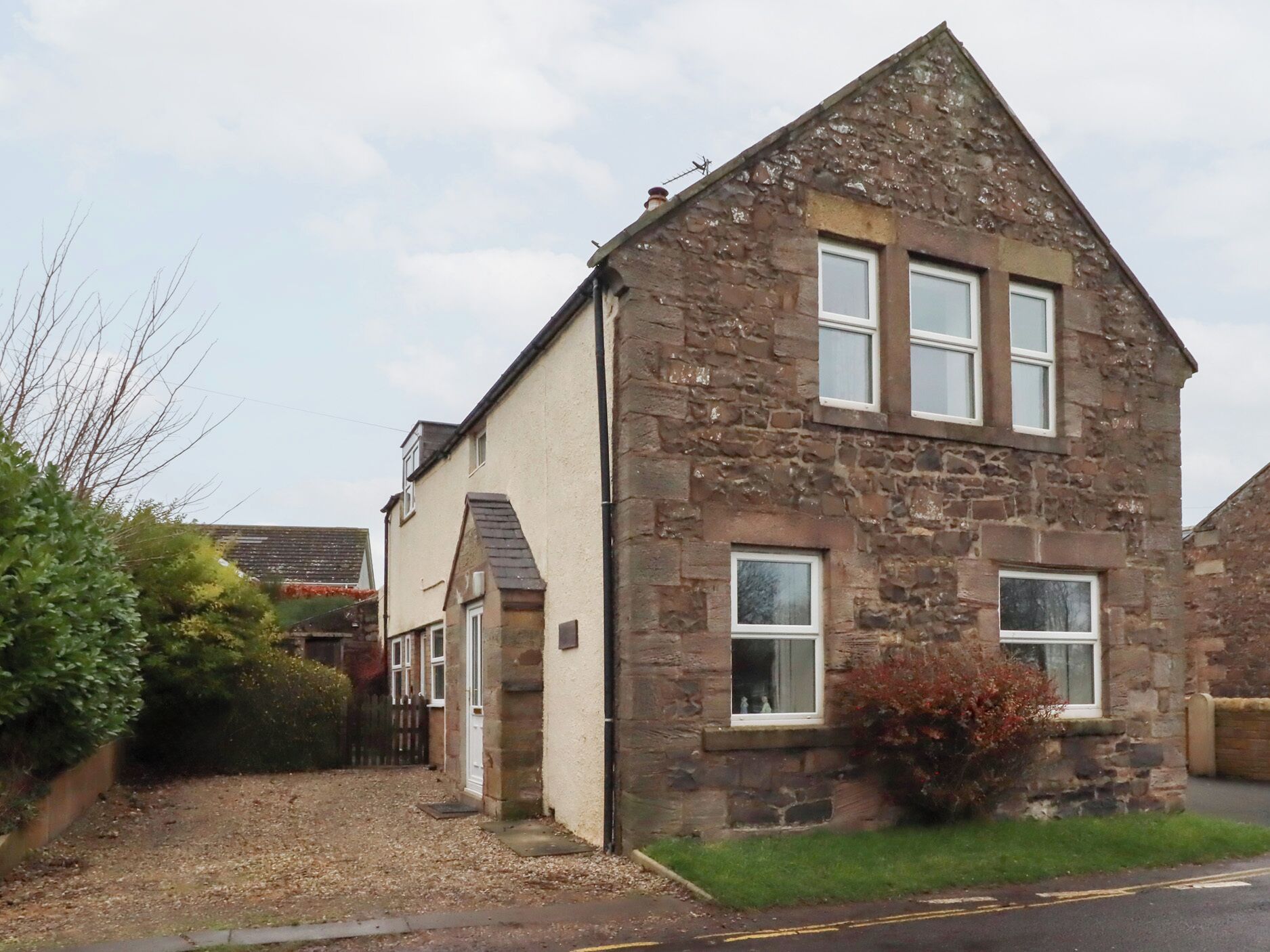 A stone house with a pitched roof, two visible windows, and a small front garden.