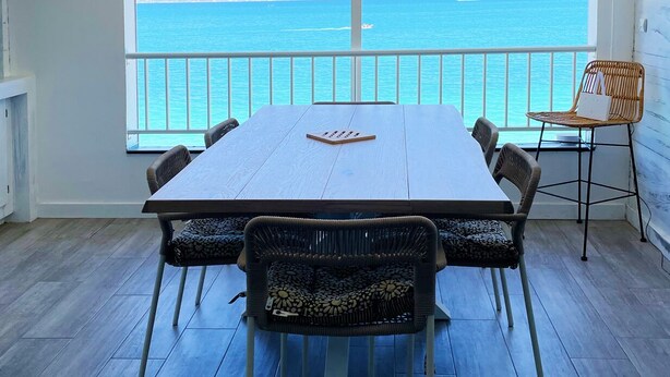 A dining area with a large table and chairs, a view of the sea, and a balcony with a railing. - Ma Case aux Antilles on Grand Case Beach! (Grand-Case)