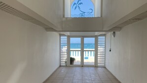 A spacious room with a tiled floor, a large window with a view of the sea, and a decorative glass panel above the window. - Ma Case aux Antilles on Grand Case Beach! (Grand-Case)