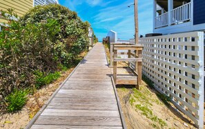 A wooden boardwalk leading to a white fence with a balcony.