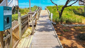 A wooden boardwalk leading to a beach area with a sign instructing to clean up after dogs.