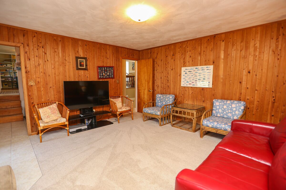 A wooden-paneled living room with a flat-screen TV, wicker chairs, a red sofa, and a small table.