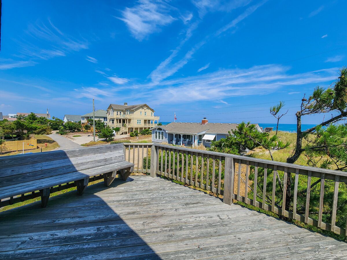 A wooden boardwalk leading to a beachfront property with a large house and a smaller building.