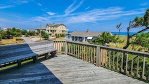 A wooden boardwalk leading to a beachfront property with a large house and a smaller building. - By Jove - Semi-Oceanfront 5 BR Beach Cottage w/Private Pool & Dogs Allowed (Southern Shores)