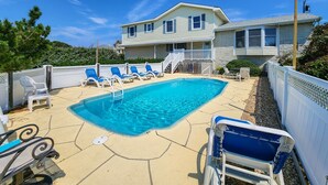 A swimming pool with lounge chairs, a covered area, and a house in the background. - By Jove - Semi-Oceanfront 5 BR Beach Cottage w/Private Pool & Dogs Allowed (Southern Shores)