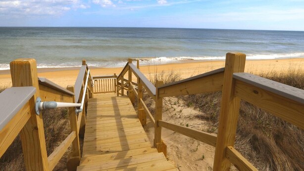 A wooden boardwalk leading to a beach with a clear view of the ocean.