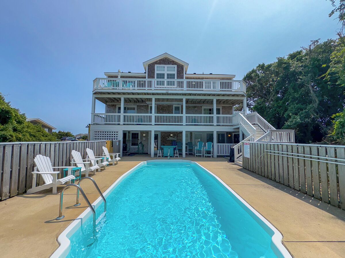 A pool area with a two-story building, outdoor seating, and a staircase leading to the upper level.