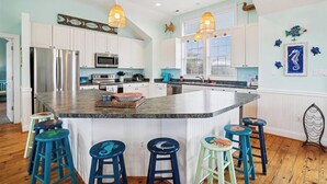 A kitchen with white cabinets, a central island with stools, stainless steel appliances, and decorative wall art.