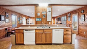 A kitchen with wooden walls, a central island with a sink, and a 'BEACH' sign. - Graves Cottage - 6 Bedroom Oceanfront Cottage w/Walkway to Beach (Southern Shores)