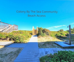 A wooden boardwalk leading to a beach with a wooden staircase and a beach access sign.