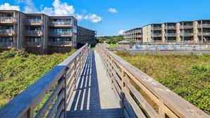 A wooden boardwalk leading to a modern apartment complex with multiple balconies. - Just Duck Inn - Bright, Cheerful, 2BR/2BA Semi-Oceanfront condo in Duck, Sleeps 4-7 (Duck)