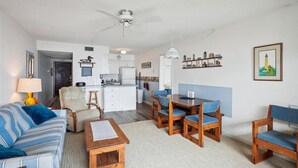 A modern living room with a sofa, coffee table, and dining area with chairs. There is a kitchen in the background with cabinets and a refrigerator. - Just Duck Inn - Bright, Cheerful, 2BR/2BA Semi-Oceanfront condo in Duck, Sleeps 4-7 (Duck)