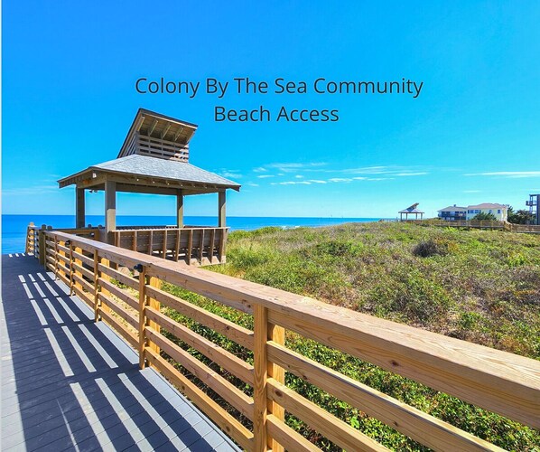 A wooden boardwalk leading to a beach with a wooden structure and a clear view of the ocean.