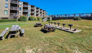 Un espace extérieur verdoyant, doté de tables de pique-nique et de barbecues, entouré d’immeubles d’habitation.