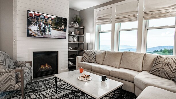 A living room with a fireplace, a sofa, a coffee table with snacks, and a TV displaying a snowy scene. - 2 Br Seneca Condo 200 Beautiful Vista Views (Snowshoe)