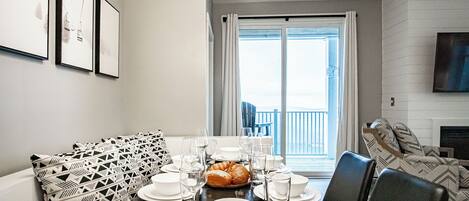 Un comedor con una mesa preparada para cuatro, un sofá estampado y vistas al exterior a través de un ventanal grande.