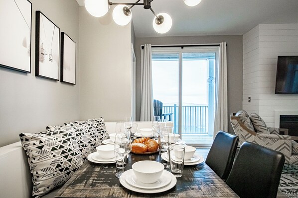 Un coin repas avec une table dressée pour quatre personnes, un canapé à motifs et une vue sur l’extérieur grâce à une grande fenêtre.