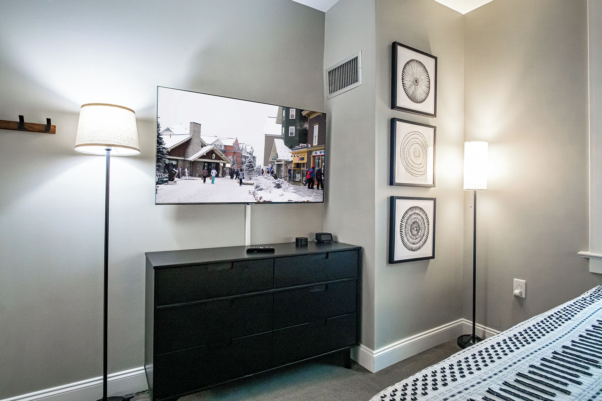 Habitación de hotel moderna con un televisor de pantalla plana grande montado en la pared, un aparador negro y una alfombra estampada.