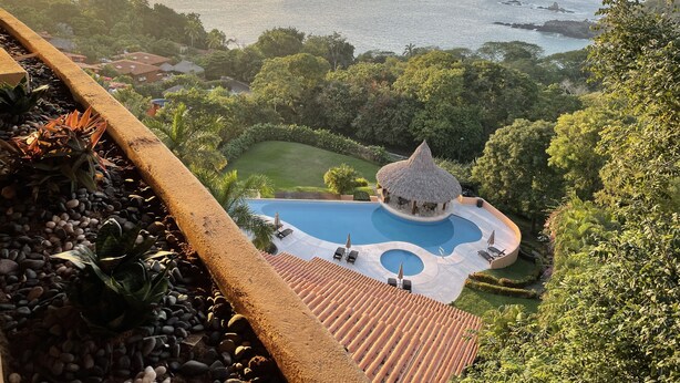 Un complexe hôtelier doté d’une piscine, d’une structure à toit de chaume et offrant une vue sur la mer.