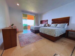 A bedroom with two beds, a desk, and a view of the outdoors.