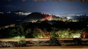 ’s Nachtzicht vanaf een balkon met rieten dak, met uitzicht op een stadsbeeld met verlichte gebouwen en een heuvel in de verte.