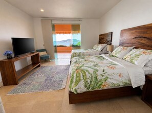 A bedroom with a TV, two beds with floral bedding, a sofa, a rug, and a view of the outdoors. - Great luxurious penthouse with private roof top pool lounge and spectacular view (Ixtapa Zihuatanejo)