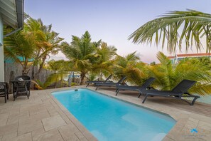 A swimming pool with lounge chairs and a table, surrounded by palm trees.