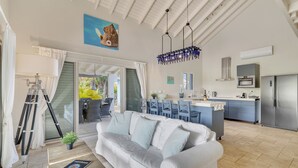 A modern kitchen with a central island, a dining area with blue chairs, and a living room with a white sofa.