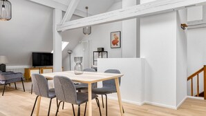 A modern dining area with a wooden table and grey upholstered chairs, a radiator, and a TV in the background. - Chic Vorstädte 2.5 Room w/ W/D & Storage, 2 min to Market, by Blueground (Basel)