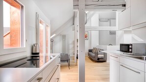 A modern kitchen with a built-in stove, a microwave, and a coffee maker. There is a gray sofa and a chair in the living area. - Chic Vorstädte 2.5 Room w/ W/D & Storage, 2 min to Market, by Blueground (Basel)