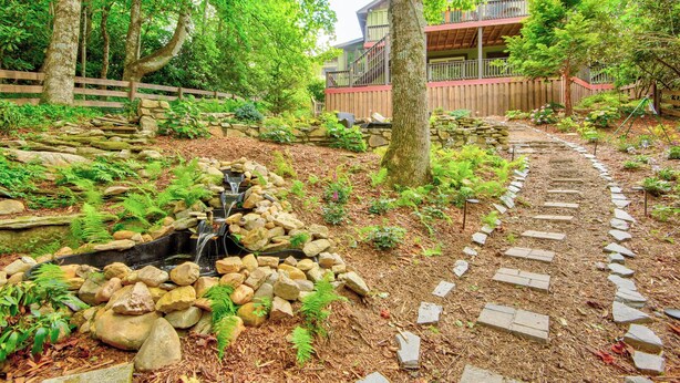 Un jardín con un sendero de piedra, una pequeña cascada y una cerca de madera.