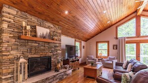 Una sala acogedora con chimenea de piedra, techo de madera y ventanas amplias.