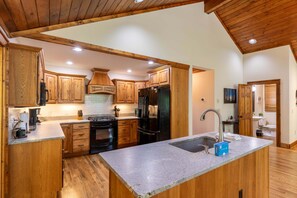 A kitchen with wooden cabinets, a black refrigerator, a stove, and a granite countertop.