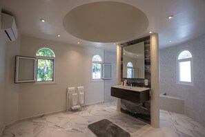 Un baño moderno con suelo de mármol, un espejo grande y dos ventanas con arcos.