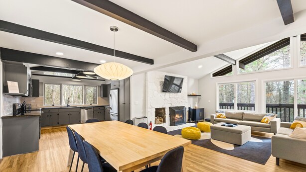 Eine moderne Küche mit einer großen Kochinsel, ein Essbereich mit Holztisch und -stühlen, ein Wohnzimmer mit Sofa und Hocker sowie ein Kamin.