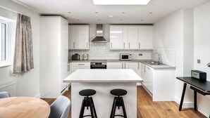 A modern kitchen with white cabinets, a central island, and a dining area with a table and bar stools. - Stylish Marylebone 2BR nr Underground, by Blueground (London)