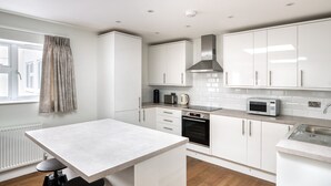 A modern kitchen with white cabinets, a built-in oven, a microwave, and a window with curtains. - Stylish Marylebone 2BR nr Underground, by Blueground (London)