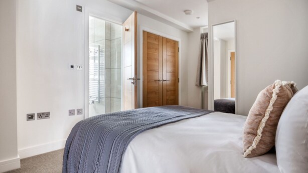 A bedroom with a large bed, a wooden wardrobe, and a glass door leading to a bathroom. - Stylish Marylebone 2BR nr Underground, by Blueground (London)