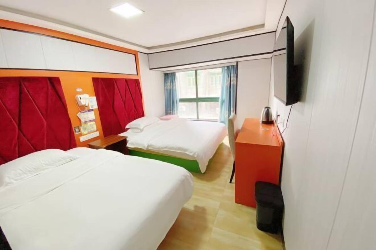 A hotel room with two beds, a desk, a TV, and a window with curtains.