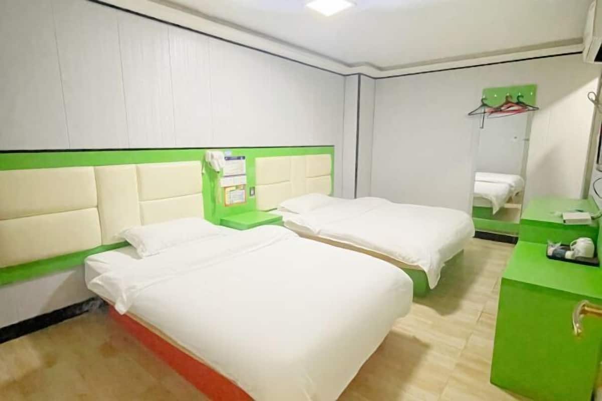 A hotel room with two beds, a green desk, a mirror, and a green wall.