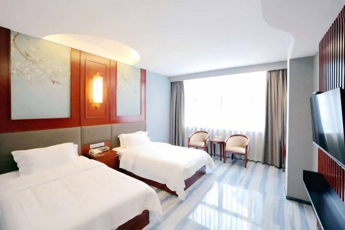 Quarto de hotel com duas camas, televisão, escrivaninha e uma cadeira.