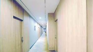 Ένας μακρύς, στενός διάδρομος με ξύλινες πόρτες και στις δύο πλευρές, που οδηγεί σε έναν κεντρικό χώρο με δάπεδο σε ανοιχτόχρωμο τόνο.