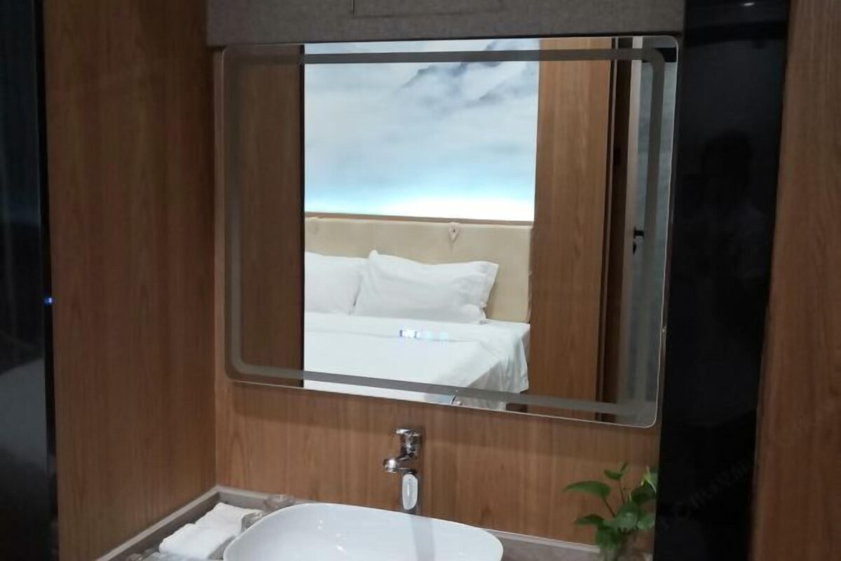 Casa de banho de hotel com um espelho grande, uma pia branca e uma vista para uma cama no reflexo.